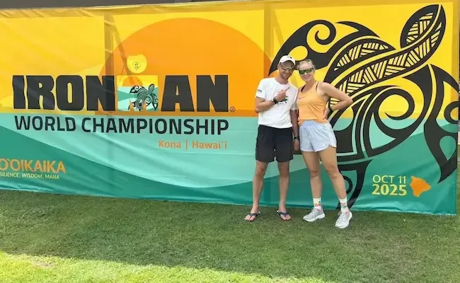 Triathlet und Lauf Coach Daniel Fahje und seine Schülerin posieren vor dem Iron Man Plakat auf Hawaii